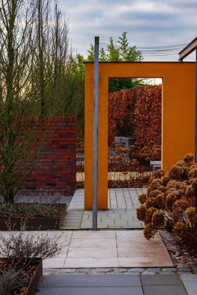 A modern garden entrance featuring vibrant orange and brick structures surrounded by autumn foliage.